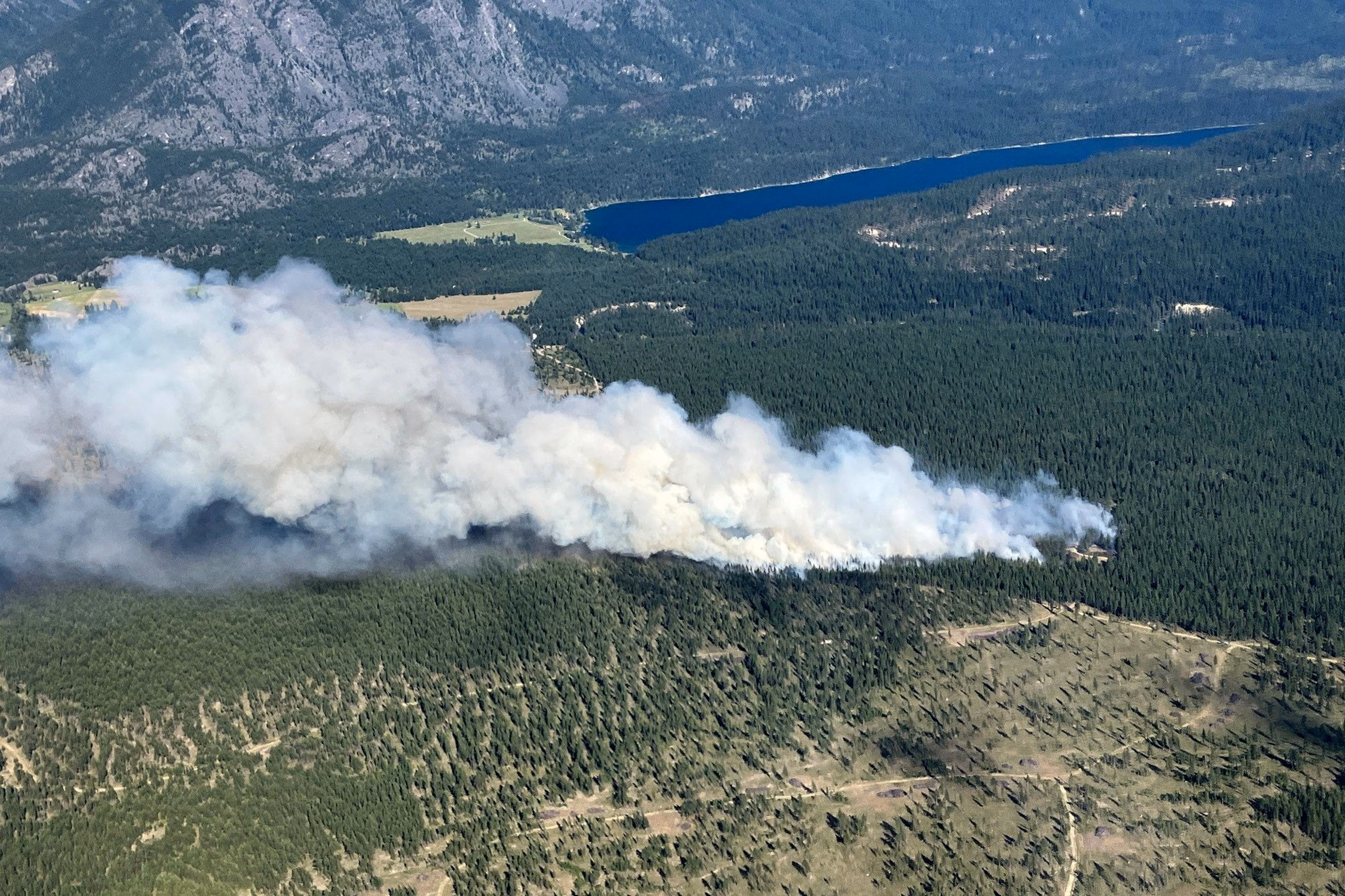 Aerial view of wildfire smoke rising over a forest near a lake